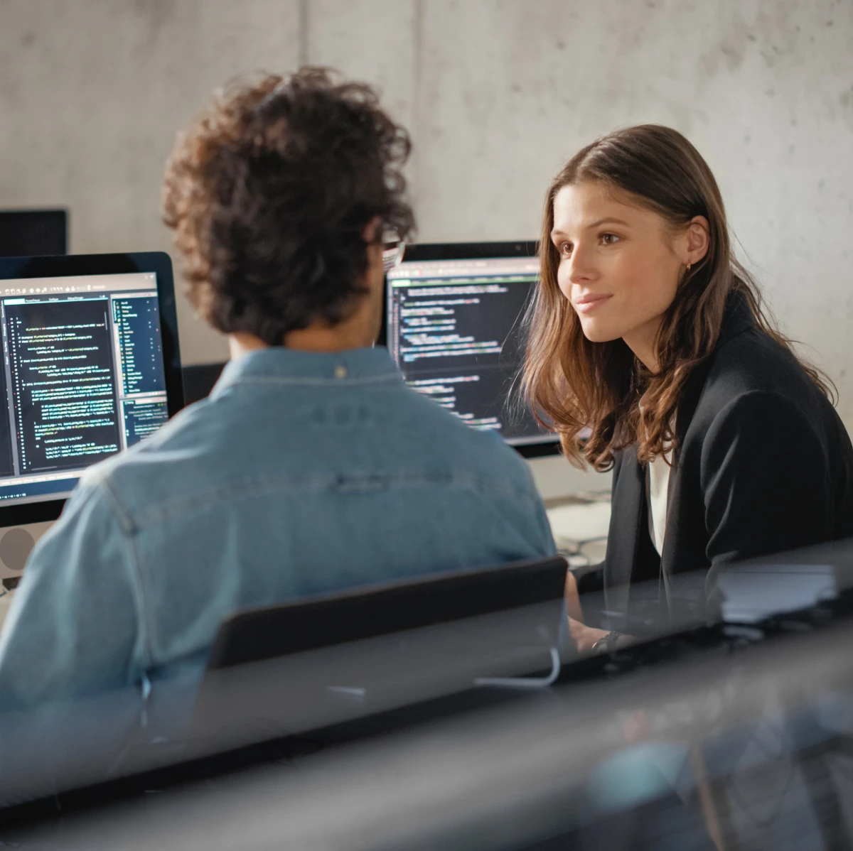 Two people discussing coding at computers.